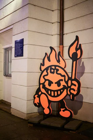 A colorful graffiti featuring a smiling character with flaming hair, holding a torch, against a building wall.