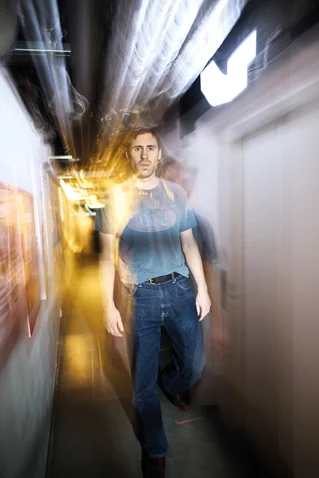 Mann geht durch einen Gang mit verschwommenen Lichteffekten, die Bewegung andeuten. Er trägt ein lässiges Outfit mit Jeans.