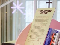 A bookshelf labeled "5,658 Banned Books" filled with various book titles. Bright, modern setting with artistic design elements.
