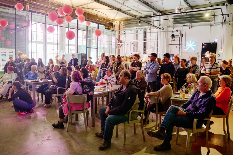 Menschenmenge in einer modernen Halle, sieht einem Event zu. Bunte Laternen hängen von der Decke, warme Beleuchtung.