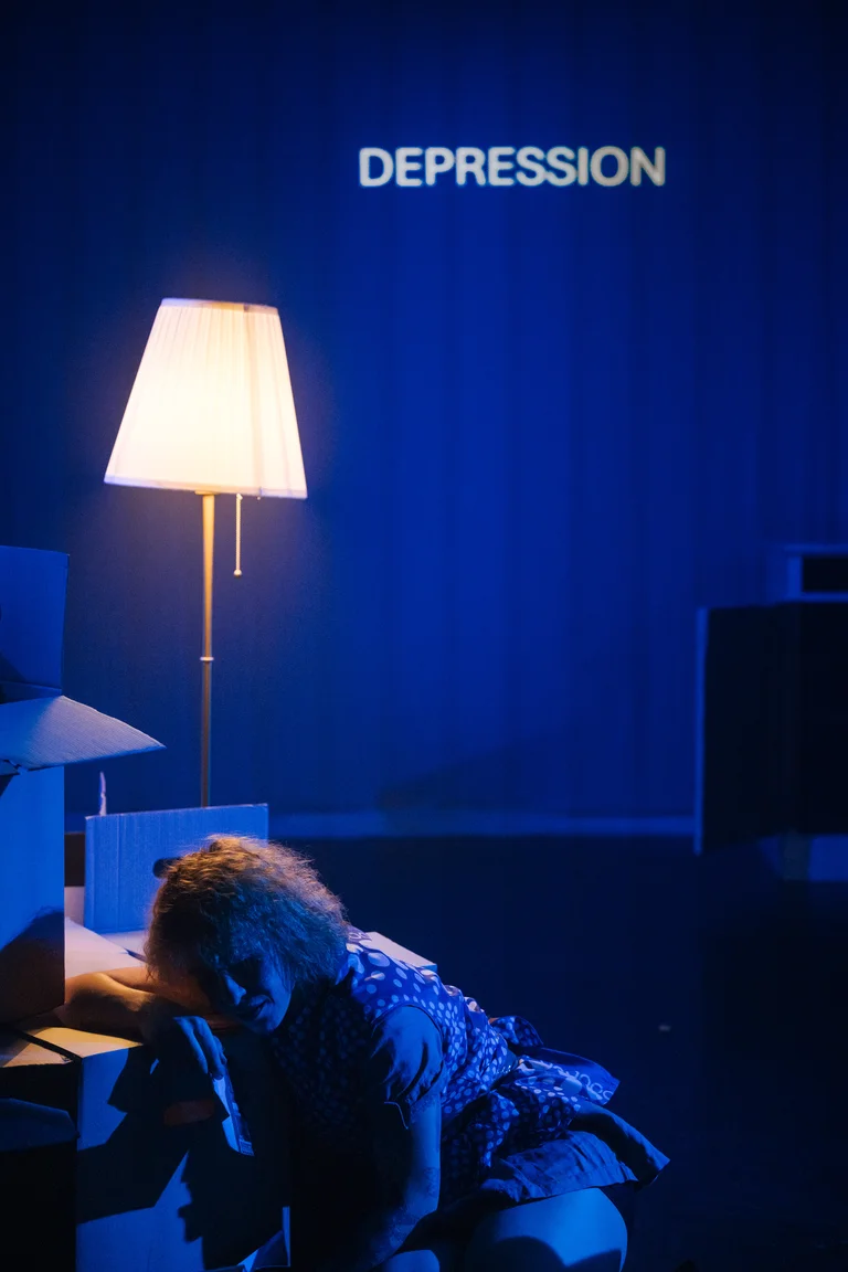 Eine Bühne mit einer Person unter einer Lampe. Das Wort "DEPRESSION" ist leuchtend an der Wand projiziert.