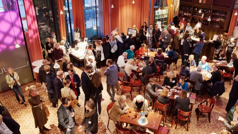 Eine gut besuchte Veranstaltung in einem eleganten Raum, mit Menschen, die sich an Tischen unterhalten und eine Bar im Hintergrund.