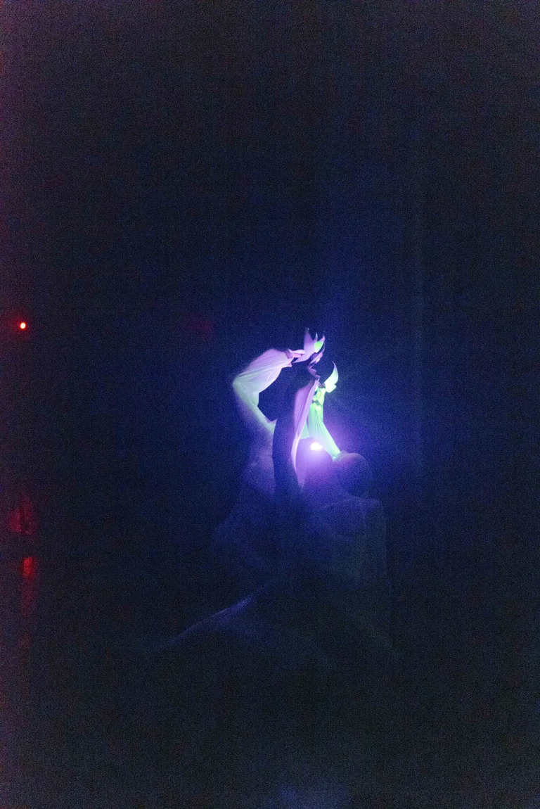 Eine beleuchtete Tänzerin bewegt sich im Dunkeln, gehüllt in fließende Stoffe. Sie wird von einem blauen Licht beleuchtet.