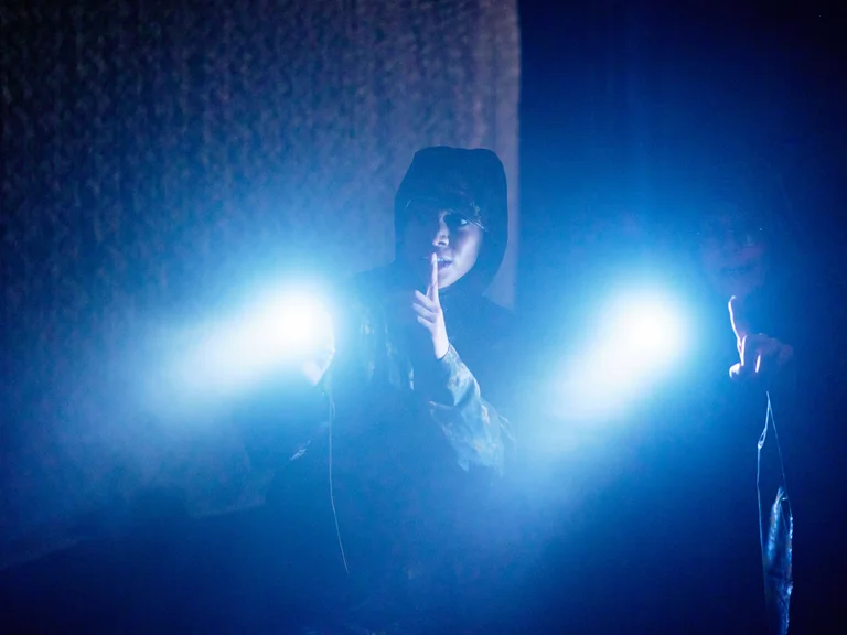 Eine Frau in einem dunklen Raum hält zwei blaue Lichter. Die Atmosphäre ist geheimnisvoll und stimmungsvoll.