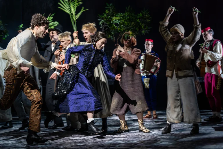 Schauspieler auf einer Bühne in historischer Kleidung, in einer lebhaften Szene mit Tanz und Interaktion. Eine dynamische Theaterproduktion.