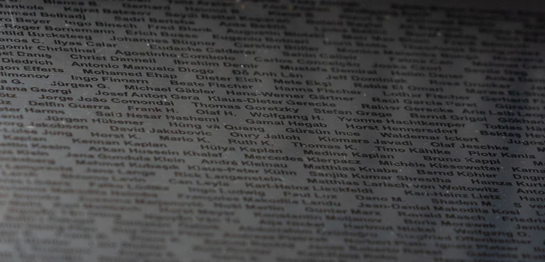Graue Wand voller eingravierter Namen in gleichmäßigen Reihen. Ein stilles Denkmal, das an zahlreiche Menschen erinnert.