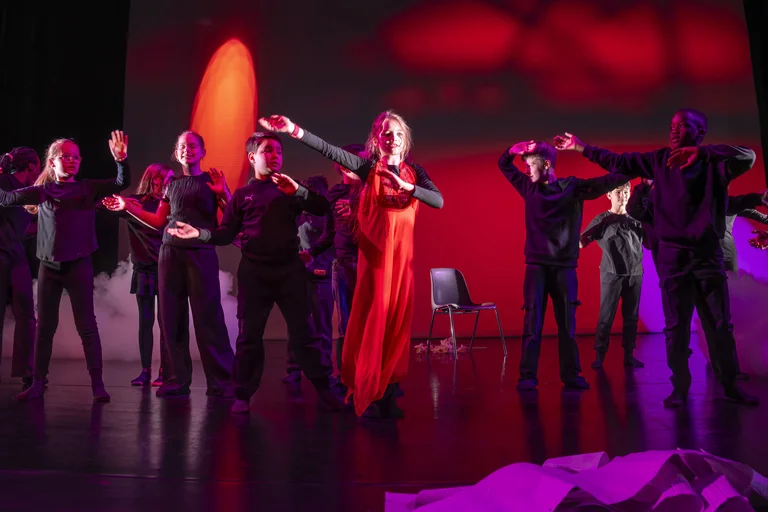 Tänzer in schwarzer Kleidung mit rotem Akzent posieren dramatisch auf einer Bühne mit intensiv rotem Licht im Hintergrund.