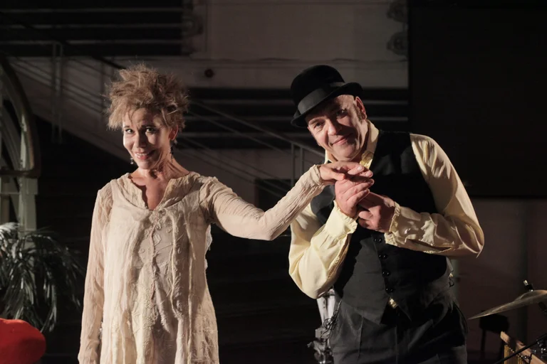 Zwei Künstler auf einer Bühne lächeln und verbeugen sich. Sie tragen Vintage-Kleidung und haben verspielte Gesichtsausdrücke.