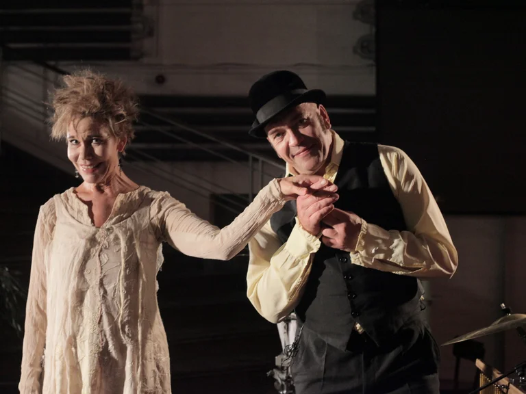 Zwei Künstler auf einer Bühne lächeln und verbeugen sich. Sie tragen Vintage-Kleidung und haben verspielte Gesichtsausdrücke.