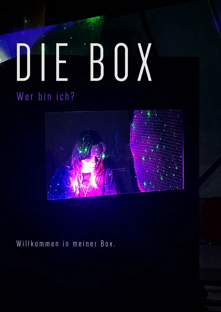 Ein Poster mit dem Titel "DIE BOX" zeigt eine beleuchtete Person in einer dunklen Umgebung. Frage: "Wer bin ich?"