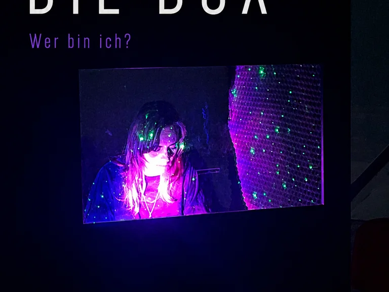 Ein Poster mit dem Titel "DIE BOX" zeigt eine beleuchtete Person in einer dunklen Umgebung. Frage: "Wer bin ich?"