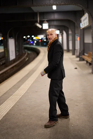 Eine Person in eleganter Kleidung steht auf einem Bahnsteig und schaut über die Schulter, während sie sich umdreht.