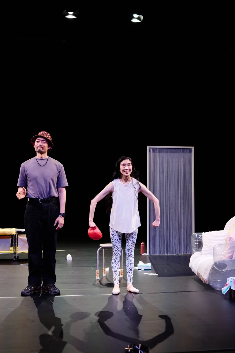 Zwei Personen auf der Bühne führen eine Theaterperformance auf. Eine trägt einen Zylinder, die andere hält einen roten Ball.