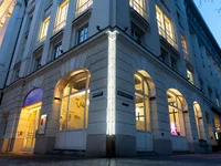 Außenansicht eines eleganten Gebäudes bei Nacht, beleuchtet mit gelbem Licht. Große Fenster und doppelte Eingänge auf jeder Seite.