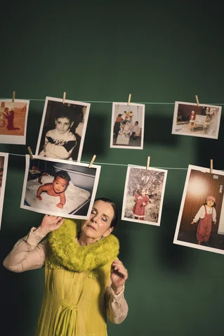 A woman in a yellow dress looks at photos of children on a clothesline. The photos show various life stages.