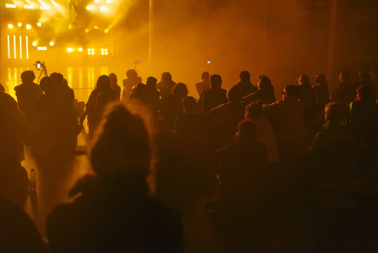 Menschenmenge genießt ein Konzert oder Festival mit intensiven, warmen Lichtern. Die Szene wirkt lebendig und dynamisch.