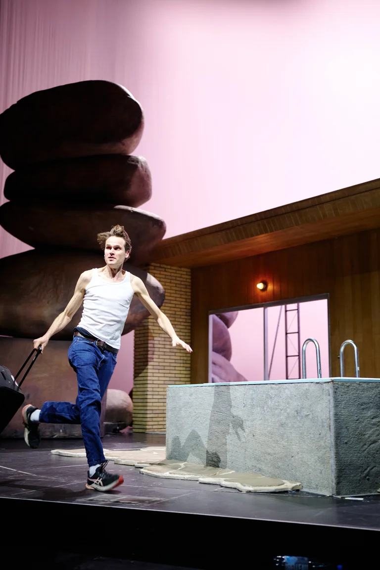 Ein Tänzer auf einer Bühne mit ungewöhnlichen Requisiten, darunter große Steine. Er trägt lässige Kleidung und performt energetisch.