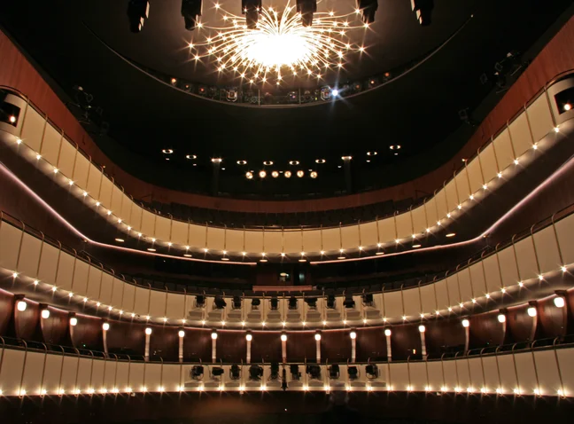 Ein prächtiger Konzertsaal mit mehreren Etagen von Sitzplätzen und einem leuchtenden Kronleuchter an der Decke.