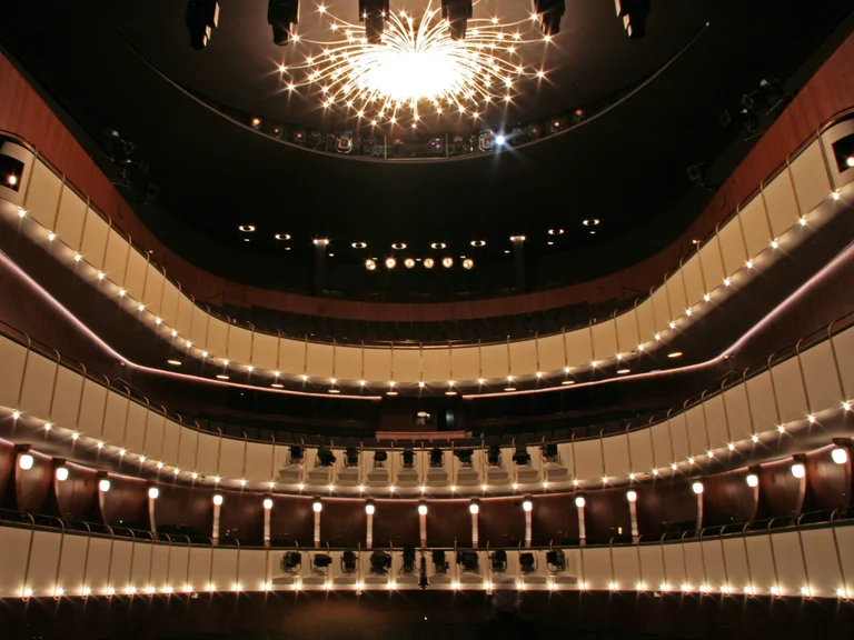 Ein prächtiger Konzertsaal mit mehreren Etagen von Sitzplätzen und einem leuchtenden Kronleuchter an der Decke.
