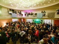 A crowded venue with attendees participating in a celebration or event. The ceiling is adorned with sparkling lights.