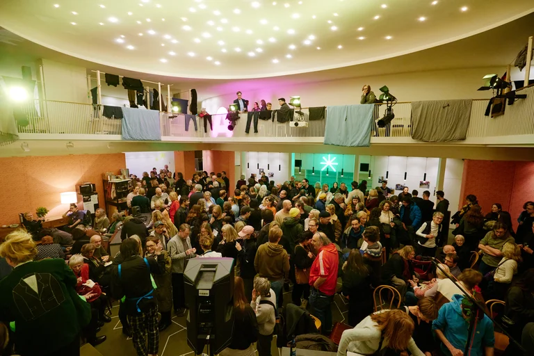 Ein voller Veranstaltungsort mit Menschen, die an einer Feier oder einem Event teilnehmen. Die Decke ist mit funkelnden Lichtern geschmückt.