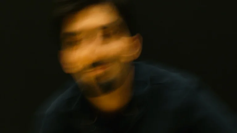 Ein unscharfes, bewegungsunschärfe Bild einer Person in dunkler Kleidung vor schwarzem Hintergrund. Das Gesicht ist nicht erkennbar.