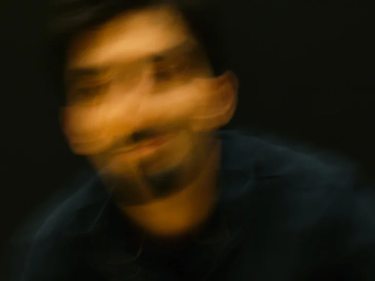 Ein unscharfes, bewegungsunschärfe Bild einer Person in dunkler Kleidung vor schwarzem Hintergrund. Das Gesicht ist nicht erkennbar.