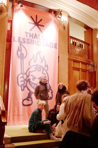 People gather in a theater foyer in front of a large banner reading "Thalia Lessingtage."