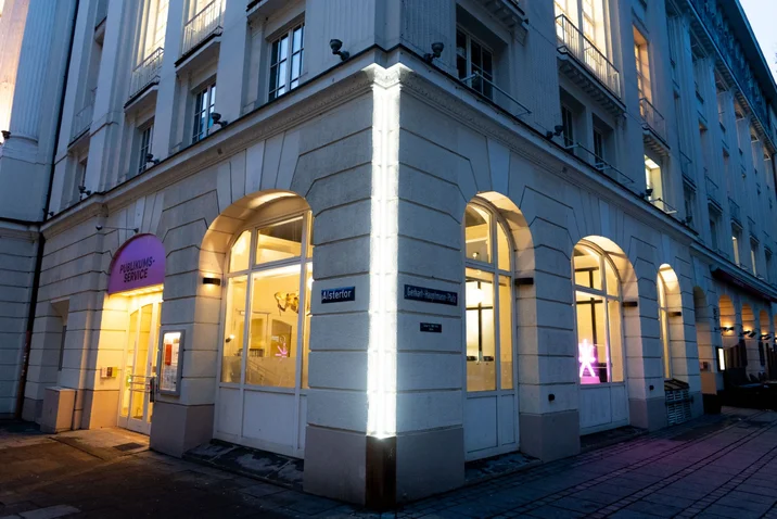 Eckgebäude mit beleuchteten Fenstern und Eingang. Architektur im Abendlicht mit lila Akzenten. Stadtatmosphäre, elegante Ästhetik.