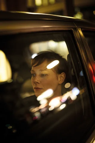 Eine Person schaut nachdenklich aus dem Fenster eines Autos, während Lichter ihr Gesicht beleuchten. Nachtatmosphäre in der Stadt.
