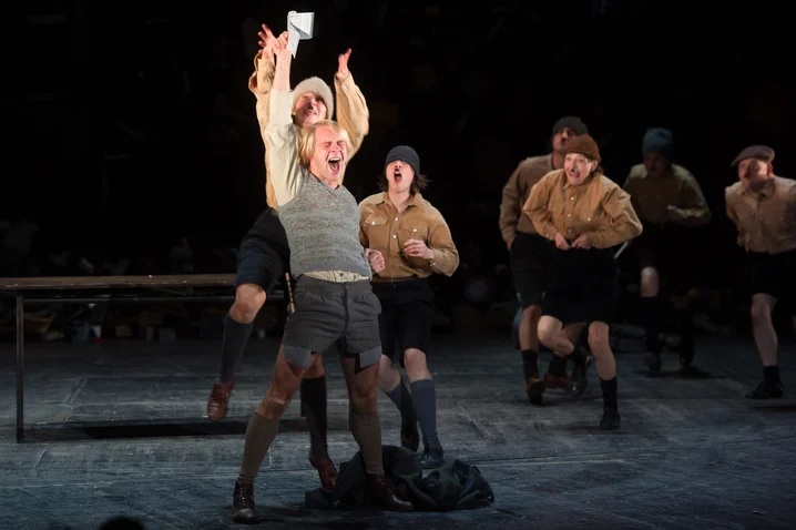 A group of actors on stage, in historical costumes, performing a dynamic scene with expressive motion and emotion.