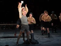 A group of actors on stage, in historical costumes, performing a dynamic scene with expressive motion and emotion.