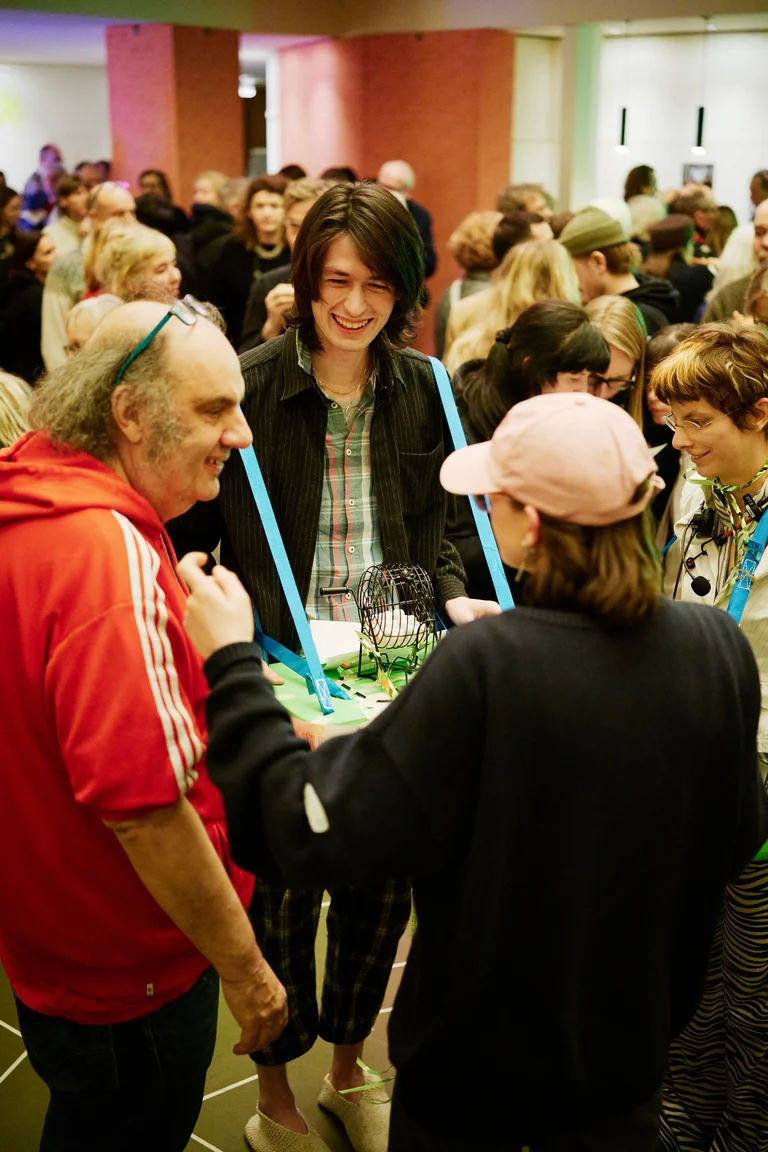 Eine fröhliche Gruppe von Menschen unterhält sich bei einer Kunstveranstaltung. Viele Menschen sind im Hintergrund zu sehen.