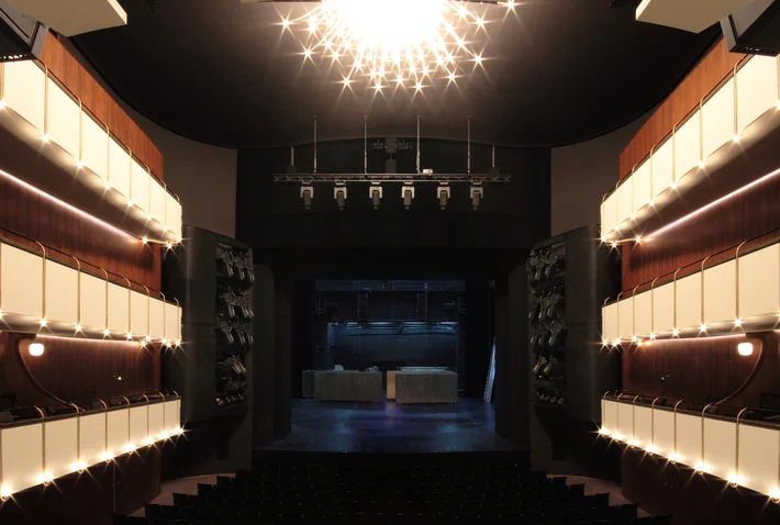 Ein elegantes Theater mit modernen Sitzreihen, gedämpfter Beleuchtung und einem großen Kronleuchter über dem Mittelgang.