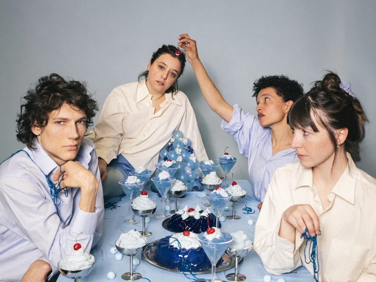 Four people in white attire sit around a table with a blue-themed setup, featuring various drinks and dishes.