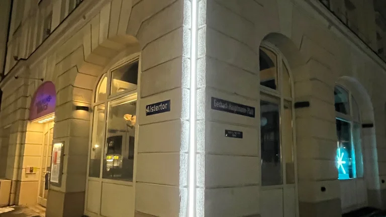 Ecke eines beleuchteten Gebäudes in der Nacht mit einem Geschäftseingang und einem Straßenschild im Vordergrund.