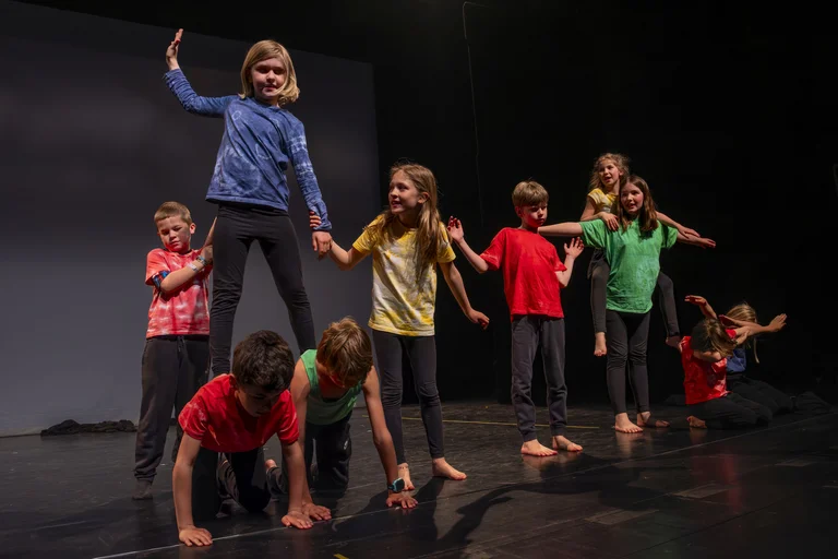 Eine Gruppe von Kindern führt eine Akrobatikaufführung auf der Bühne auf. Sie tragen bunte Kleidung und bilden Pyramiden.