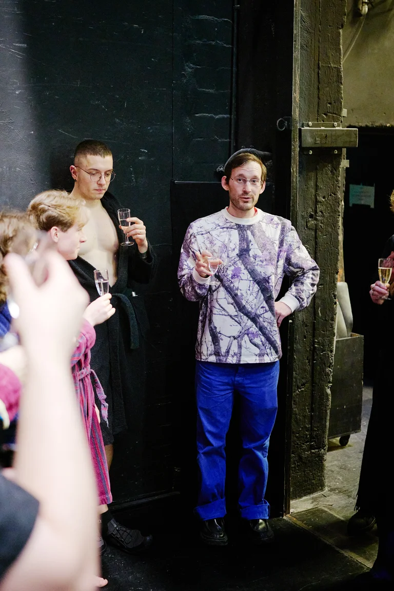 Menschen in einem entspannten, geselligen Umfeld, einige mit Getränken in der Hand. Eine Person spricht zu einer kleinen Gruppe.